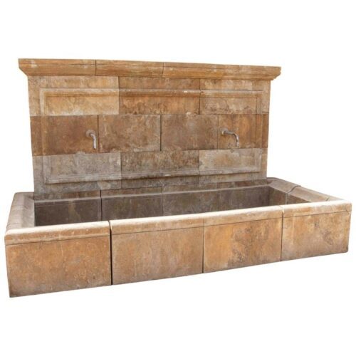 Fuente monumental de pared de piedra tallada con doble caño y una gran pileta.